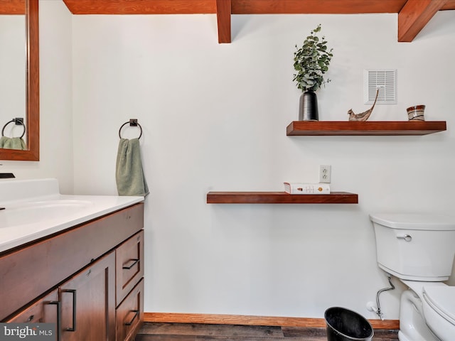 half bathroom with visible vents, beam ceiling, toilet, and vanity
