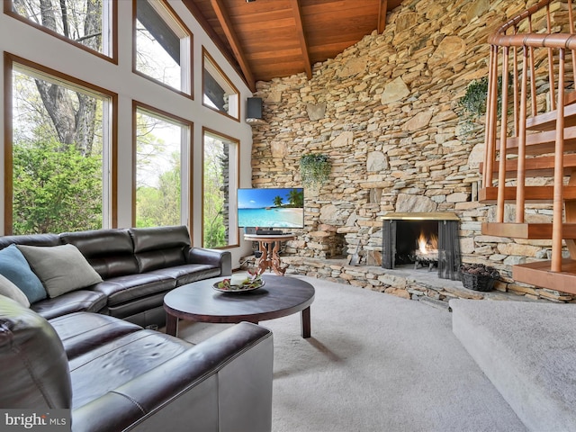 living area featuring beam ceiling, a stone fireplace, high vaulted ceiling, wooden ceiling, and carpet