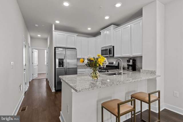 kitchen featuring white cabinets, a peninsula, appliances with stainless steel finishes, and a kitchen bar