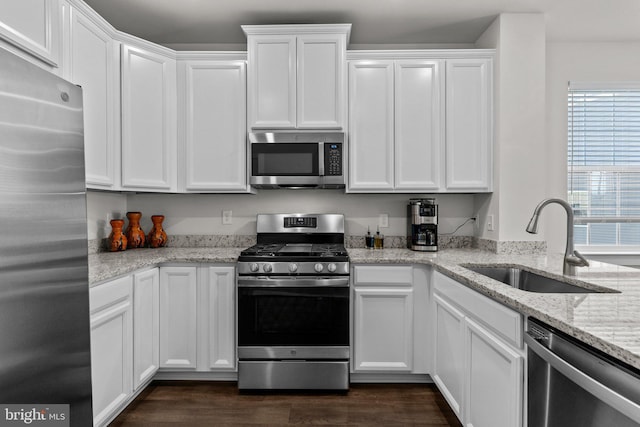 kitchen featuring dark wood-style flooring, light stone countertops, white cabinetry, a sink, and appliances with stainless steel finishes