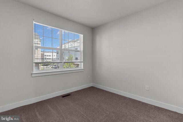 spare room featuring baseboards, visible vents, a wealth of natural light, and dark carpet