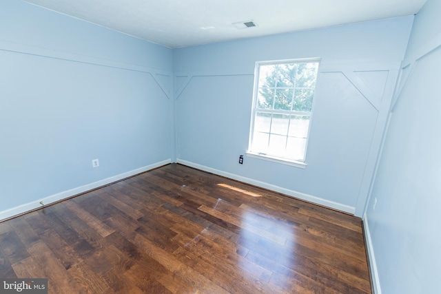 unfurnished room featuring baseboards, dark wood-style floors, and visible vents