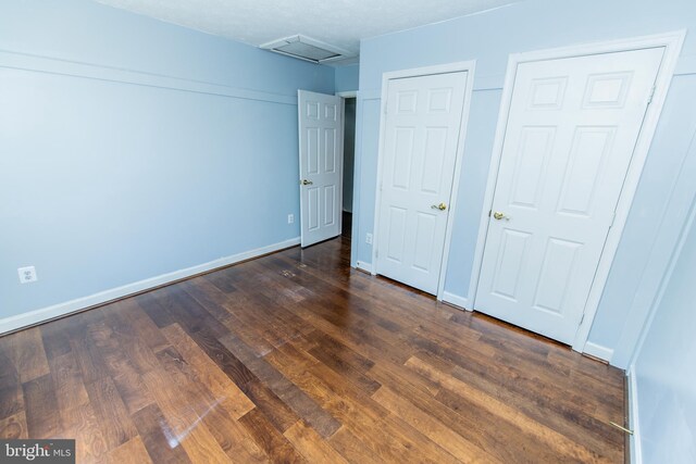 unfurnished bedroom featuring baseboards, attic access, and dark wood-style floors