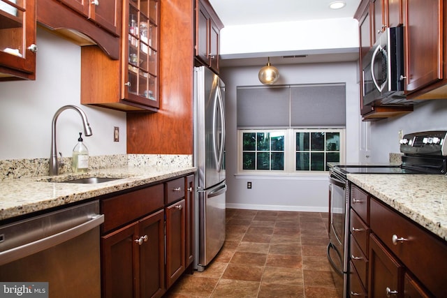 kitchen featuring baseboards, light stone countertops, stainless steel appliances, glass insert cabinets, and a sink