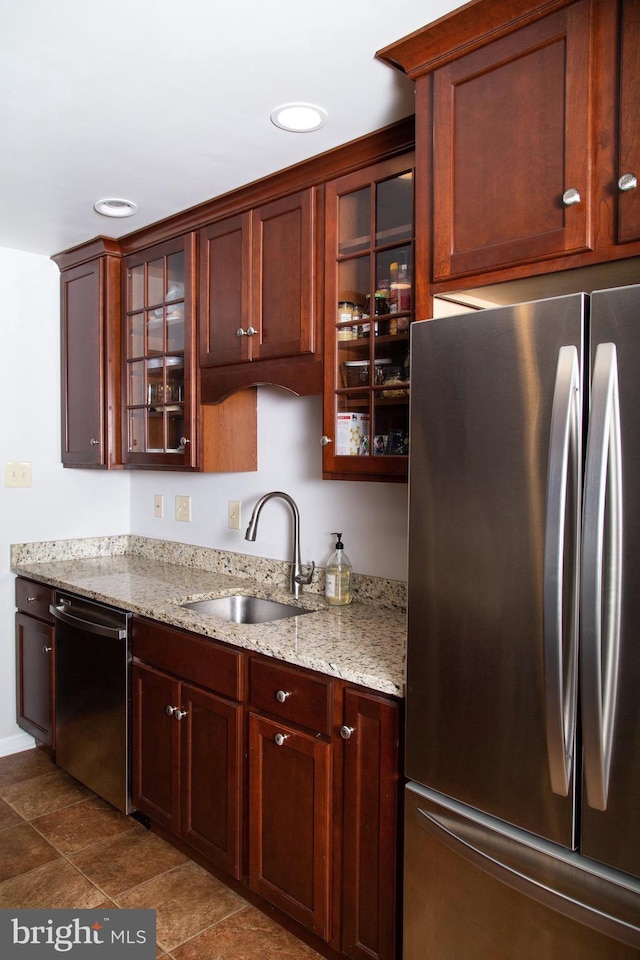 kitchen featuring glass insert cabinets, a sink, light stone counters, and appliances with stainless steel finishes