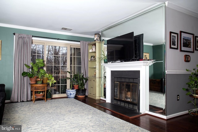 unfurnished living room with a glass covered fireplace, baseboards, visible vents, ornamental molding, and hardwood / wood-style floors