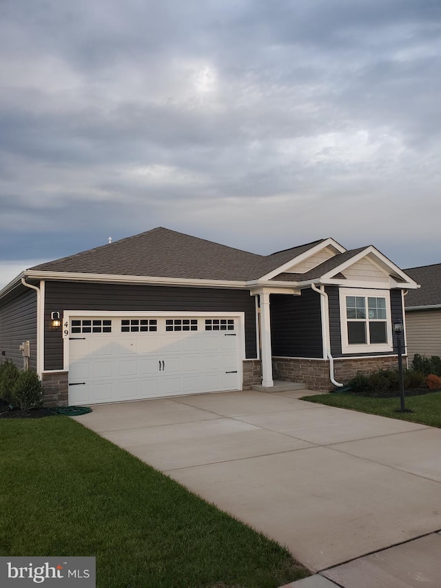 craftsman house featuring concrete driveway, roof with shingles, an attached garage, stone siding, and a front yard