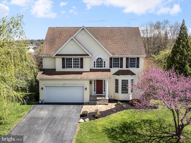 traditional-style home with a shingled roof, driveway, and a garage
