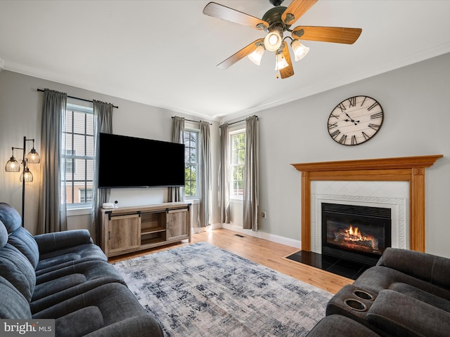 living area featuring crown molding, wood finished floors, ceiling fan, a tiled fireplace, and baseboards
