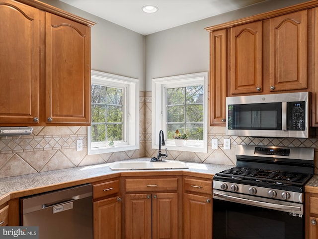 kitchen with brown cabinetry, a wealth of natural light, appliances with stainless steel finishes, and a sink