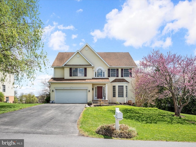 traditional-style home with a garage, driveway, a shingled roof, and a front yard