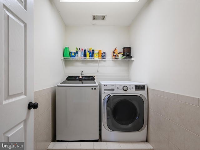 laundry room featuring a wainscoted wall, tile walls, visible vents, separate washer and dryer, and laundry area
