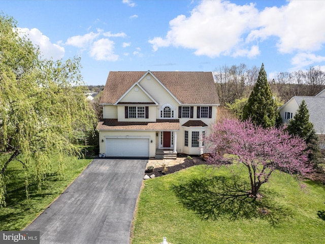 traditional-style house featuring a front lawn, driveway, roof with shingles, and a garage