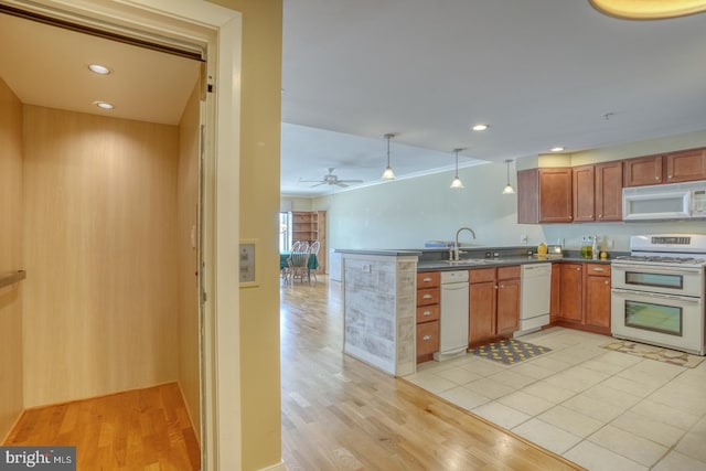 kitchen with white appliances, dark countertops, a sink, light wood-type flooring, and a peninsula