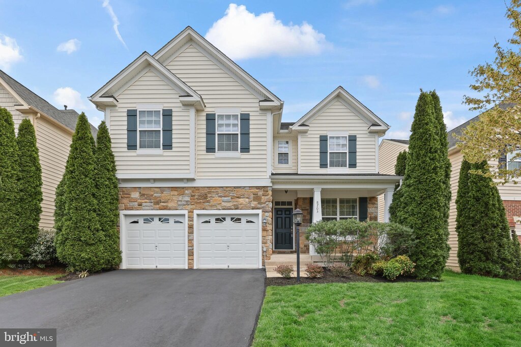 craftsman inspired home with driveway, stone siding, an attached garage, a front lawn, and a porch