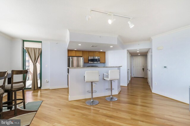 414 Water St Unit 1802, Baltimore, MD 21202 - kitchen featuring a breakfast bar area, brown cabinetry, light wood-style flooring, stainless steel appliances, and ornamental molding