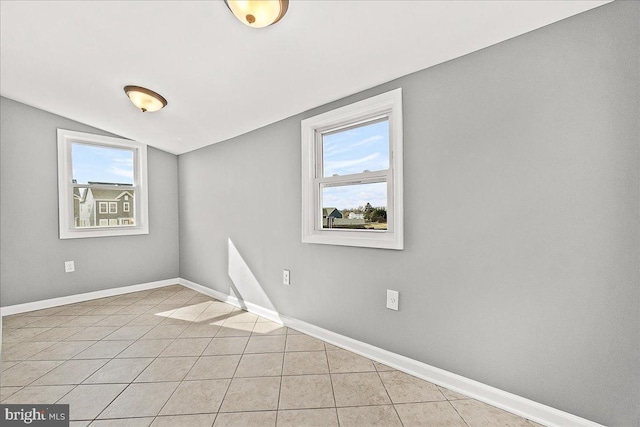 unfurnished room with plenty of natural light, baseboards, vaulted ceiling, and light tile patterned floors