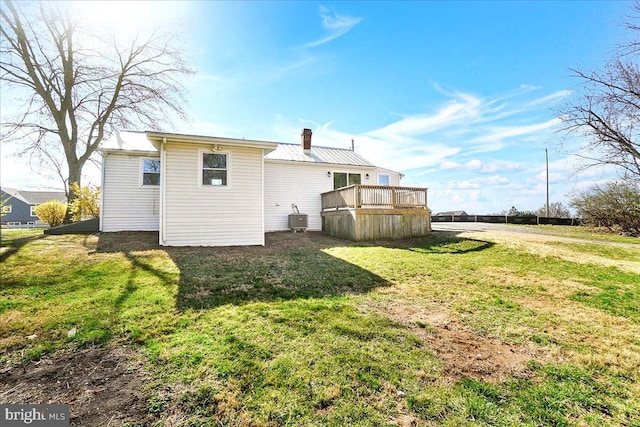 back of property featuring a wooden deck, a chimney, central air condition unit, and a lawn