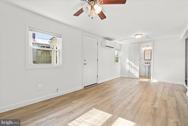 unfurnished living room with a wall mounted AC, light wood finished floors, baseboards, a ceiling fan, and a sink
