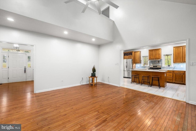 unfurnished living room featuring light wood-style floors, recessed lighting, a towering ceiling, and baseboards