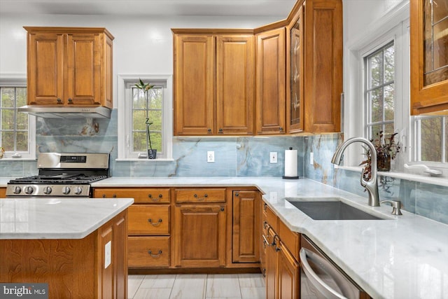 kitchen with stainless steel appliances, under cabinet range hood, brown cabinets, and a sink