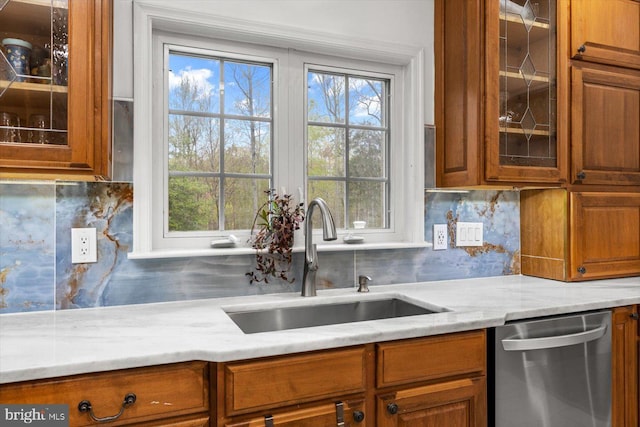 kitchen featuring brown cabinetry, stainless steel dishwasher, a sink, and a wealth of natural light