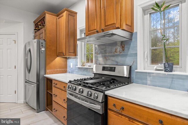 kitchen featuring brown cabinets, appliances with stainless steel finishes, decorative backsplash, and under cabinet range hood