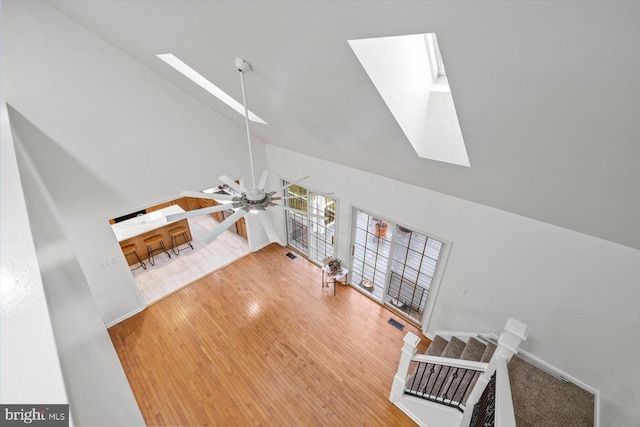 unfurnished living room with a skylight, wood finished floors, high vaulted ceiling, and visible vents