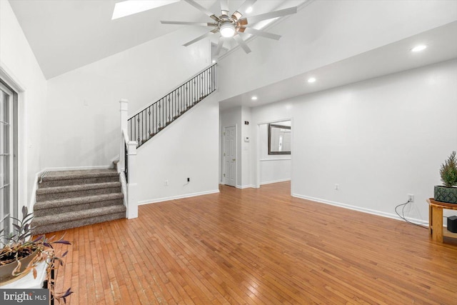 unfurnished living room featuring light wood-style floors, high vaulted ceiling, a ceiling fan, stairs, and baseboards