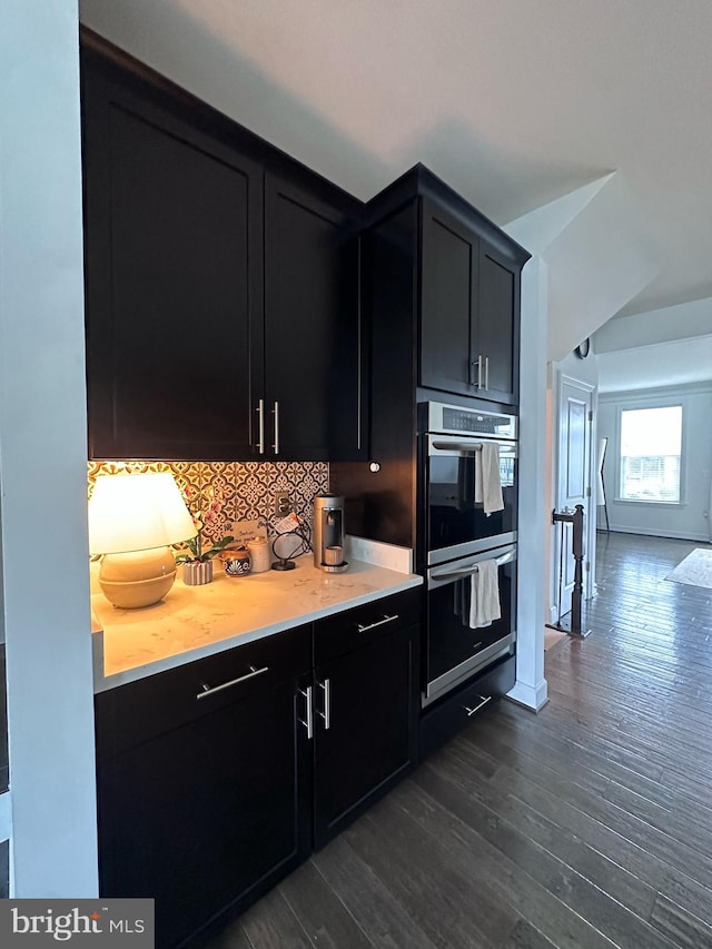 8676 Underhill Ln, Manassas, VA 20112 - kitchen featuring dark wood-style flooring, light countertops, dark cabinets, double oven, and decorative backsplash