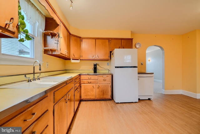 kitchen with arched walkways, a sink, freestanding refrigerator, brown cabinets, and light wood-style flooring