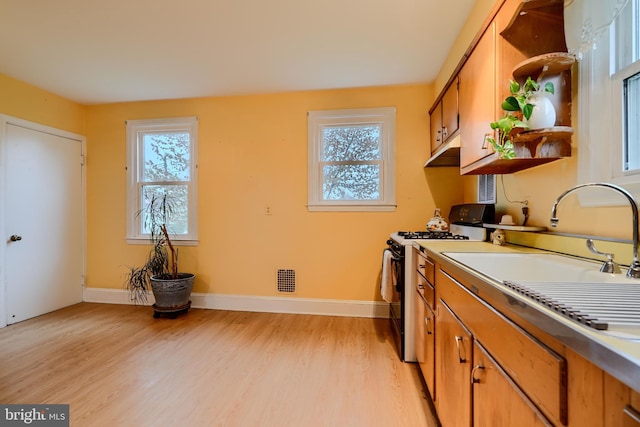 kitchen with light wood-type flooring, gas range, a sink, brown cabinets, and baseboards