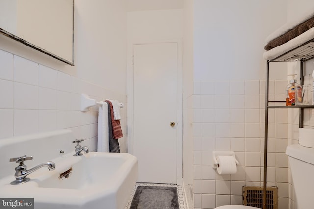 bathroom with toilet, a sink, and tile walls