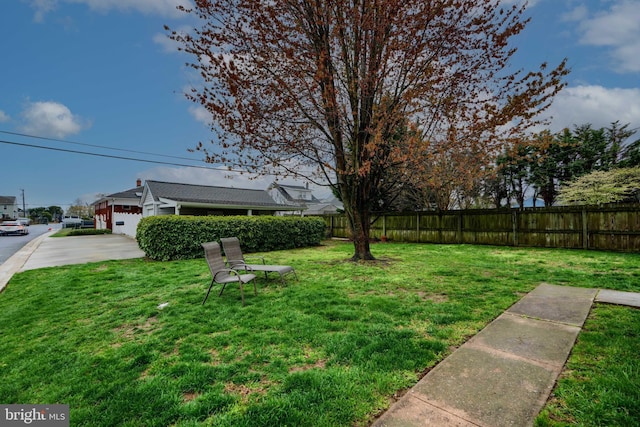 view of yard with an attached garage, driveway, and fence