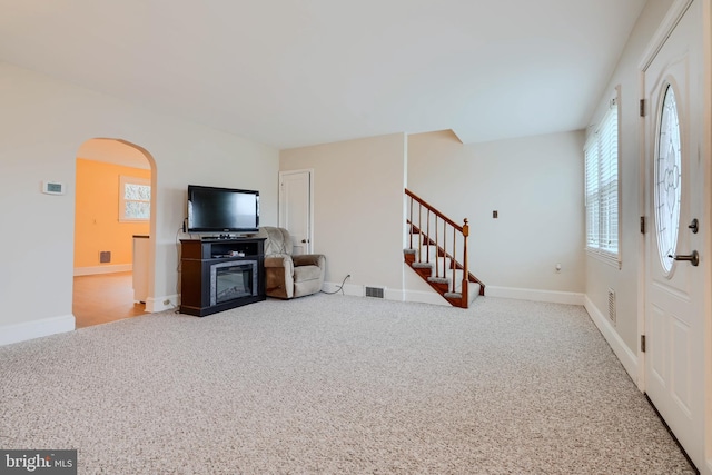 carpeted living area with arched walkways, visible vents, baseboards, and stairs