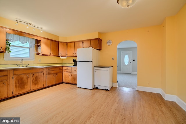 kitchen with arched walkways, brown cabinets, a sink, and freestanding refrigerator