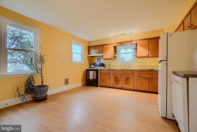 kitchen featuring visible vents, light wood-style floors, under cabinet range hood, brown cabinetry, and gas range oven