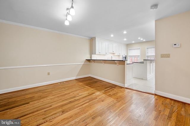 922 Fell St, Baltimore, MD 21231 - kitchen with a kitchen breakfast bar, baseboards, a peninsula, dark countertops, and light wood finished floors