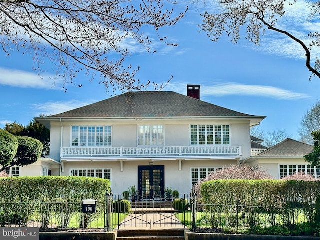 back of property with a fenced front yard, french doors, stucco siding, and a balcony