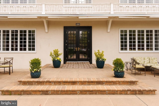 property entrance featuring french doors, stucco siding, and a balcony