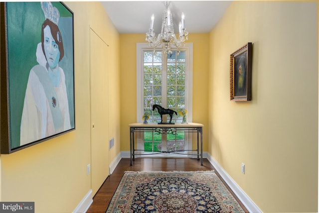 hallway with dark wood-type flooring, visible vents, baseboards, and a chandelier