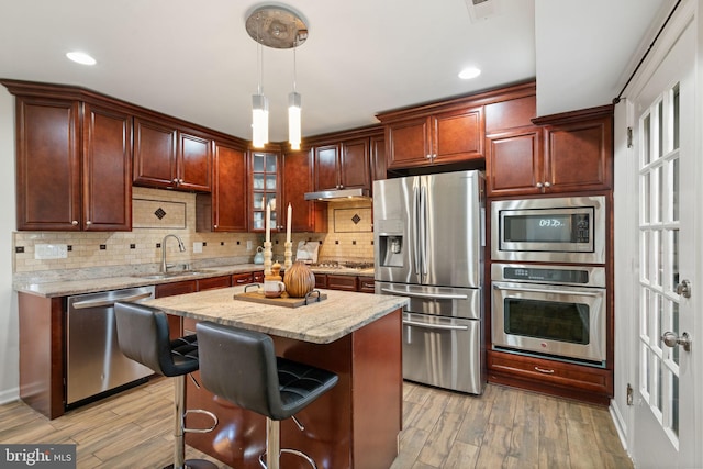 kitchen with stainless steel appliances, a sink, backsplash, light wood-style floors, and under cabinet range hood
