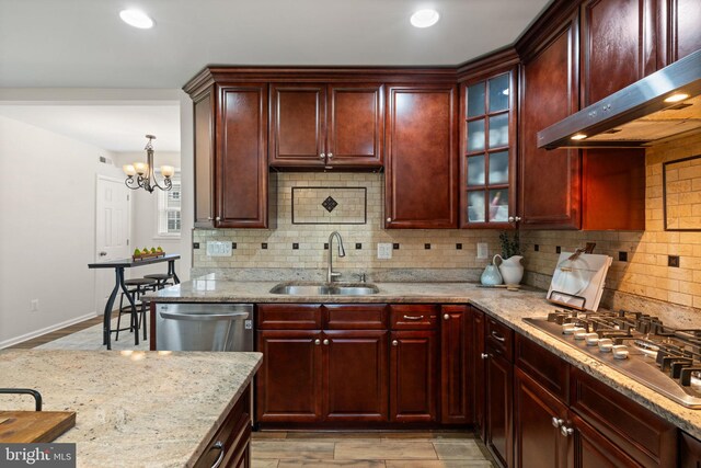 kitchen featuring stainless steel appliances, backsplash, wall chimney range hood, reddish brown cabinets, and a sink