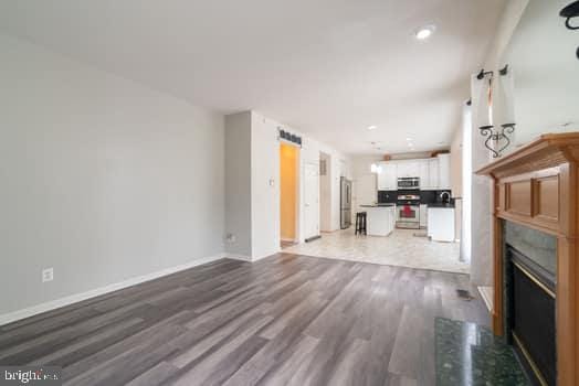 17661 Avenel Ln, Dumfries, VA 22026 - unfurnished living room featuring wood finished floors, a glass covered fireplace, baseboards, and recessed lighting