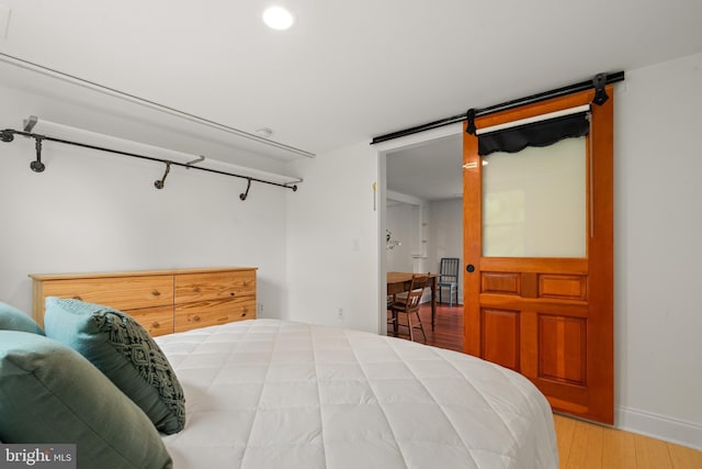 bedroom featuring a barn door, wood finished floors, baseboards, and recessed lighting