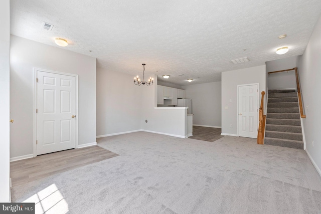 unfurnished living room featuring a textured ceiling, visible vents, a chandelier, and stairway