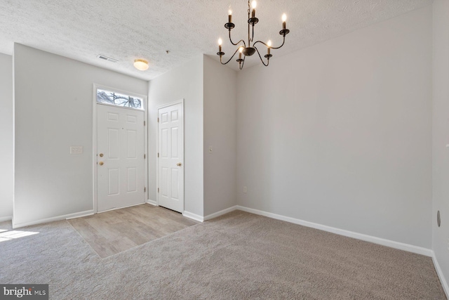 foyer entrance featuring a textured ceiling, visible vents, carpet, baseboards, and an inviting chandelier