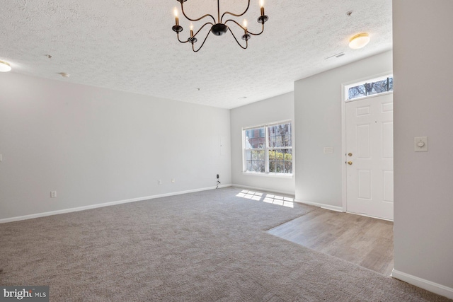 entryway with carpet floors, a notable chandelier, baseboards, and a textured ceiling