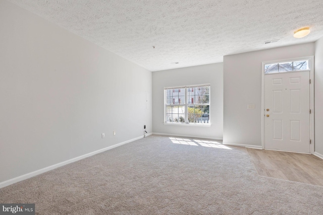 carpeted foyer entrance featuring baseboards and a textured ceiling