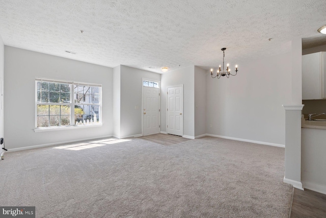 unfurnished living room with an inviting chandelier, carpet, baseboards, a textured ceiling, and a sink